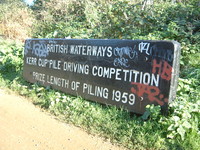 A sign by the Grand Union Canal that says 'British Waterways Kerr Cup Pile Driving Competition, Prize Length of Piling 1959'
