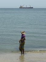 A man fishing in Santa Marta with a container ship in the background